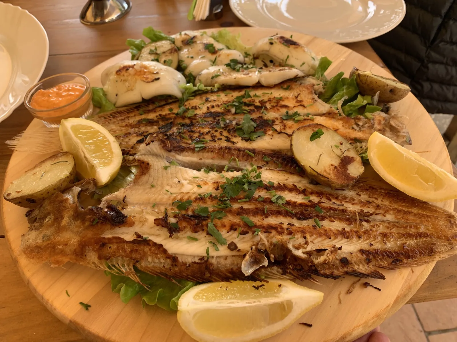 Grilled sole on a wooden board with lemon and potatoes